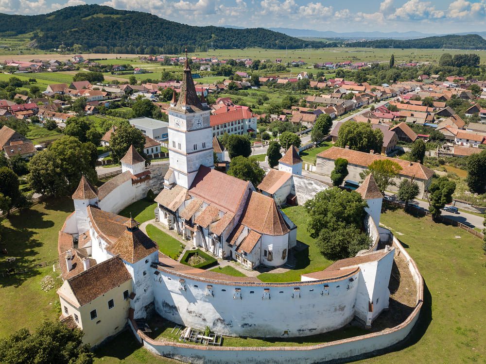 Aerial view of the Viscri fortified church surrounded by village houses and green hills in the Transylvanian countryside, Romania.