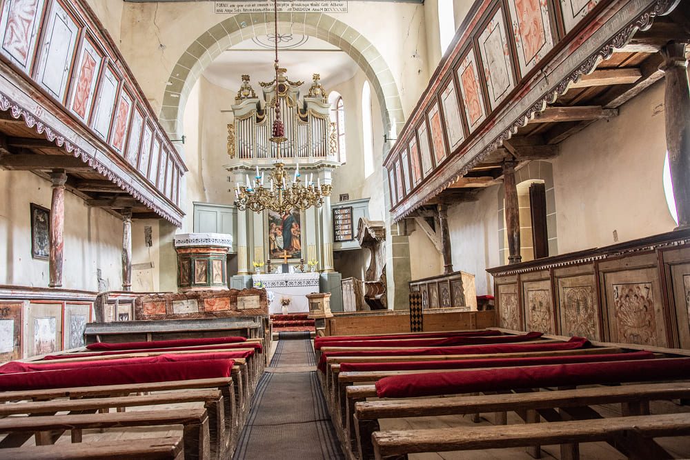 Interior of the historic Viscri fortified church featuring traditional wooden pews, painted galleries, and an ornate pipe organ.