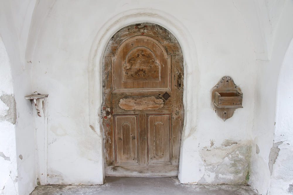 Antique carved wooden door and traditional wall fixtures framed by a bright white, lime-washed entryway at the historic Viscri fortified church.